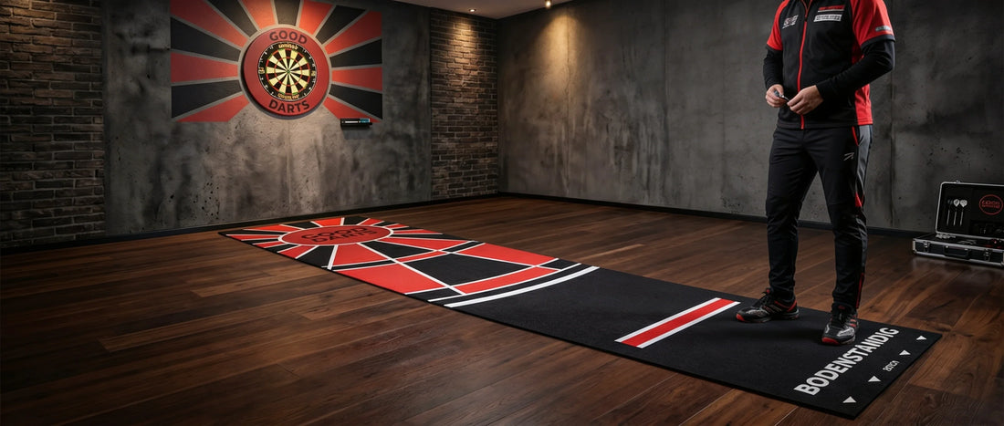 Professionelle Bodenständig Darts-Teppichmatte in Schwarz und Rot mit Abwurflinie (Oche) auf Holzboden, im Hintergrund eine Dartscheibe an einer Klinkerwand und ein Dartspieler.