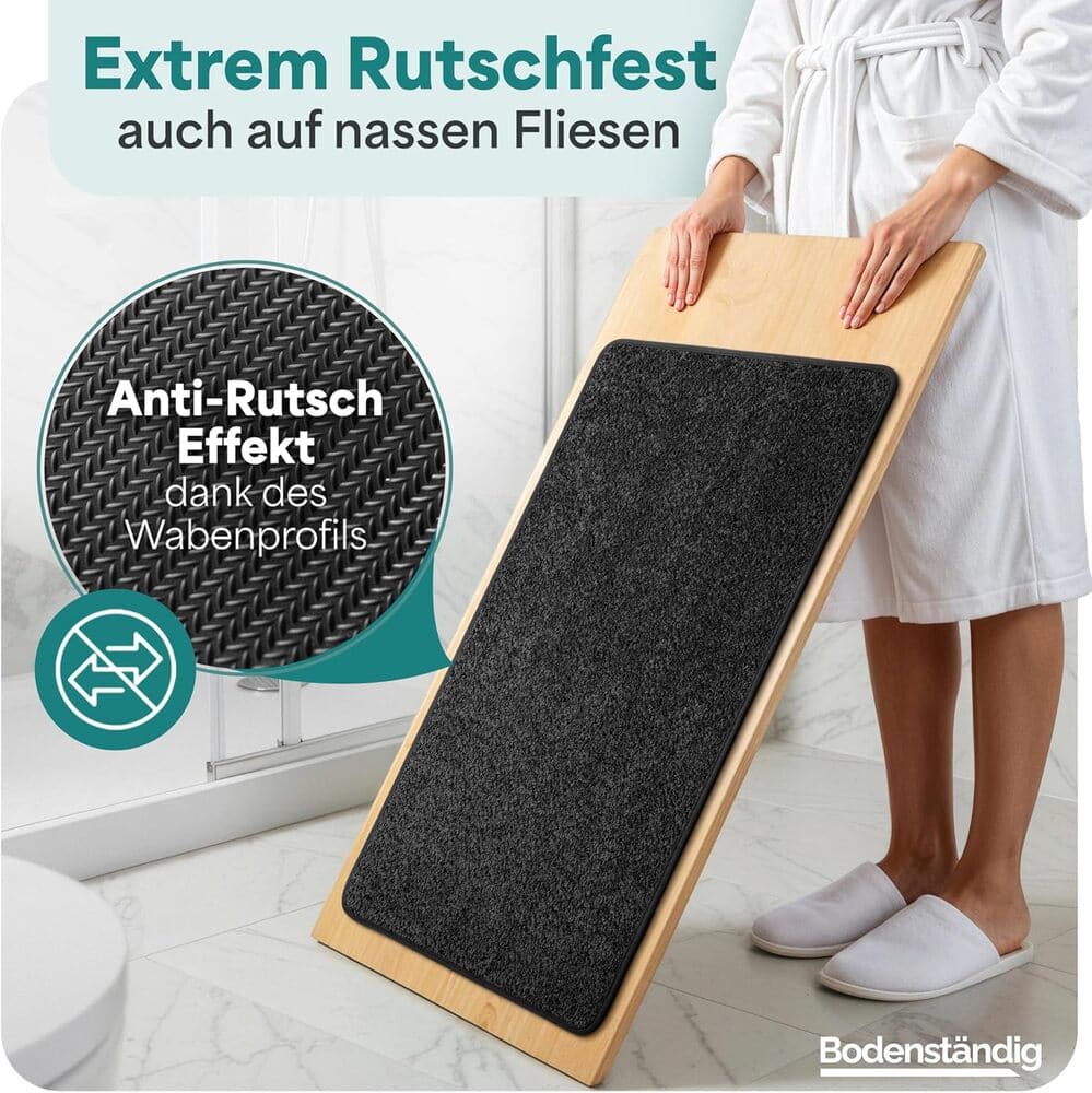 Rutschfeste schwarze Badematte auf schraeger Holzplatte demonstriert starken Halt durch Wabenprofil, ideal fuer nasse Fliesen im Badezimmer