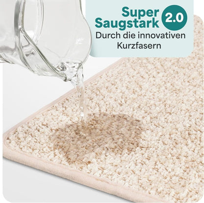 Wasser wird auf eine beige Badematte gegossen und sofort absorbiert, dank innovativer Kurzfasern mit starker Saugkraft fuer das Badezimmer