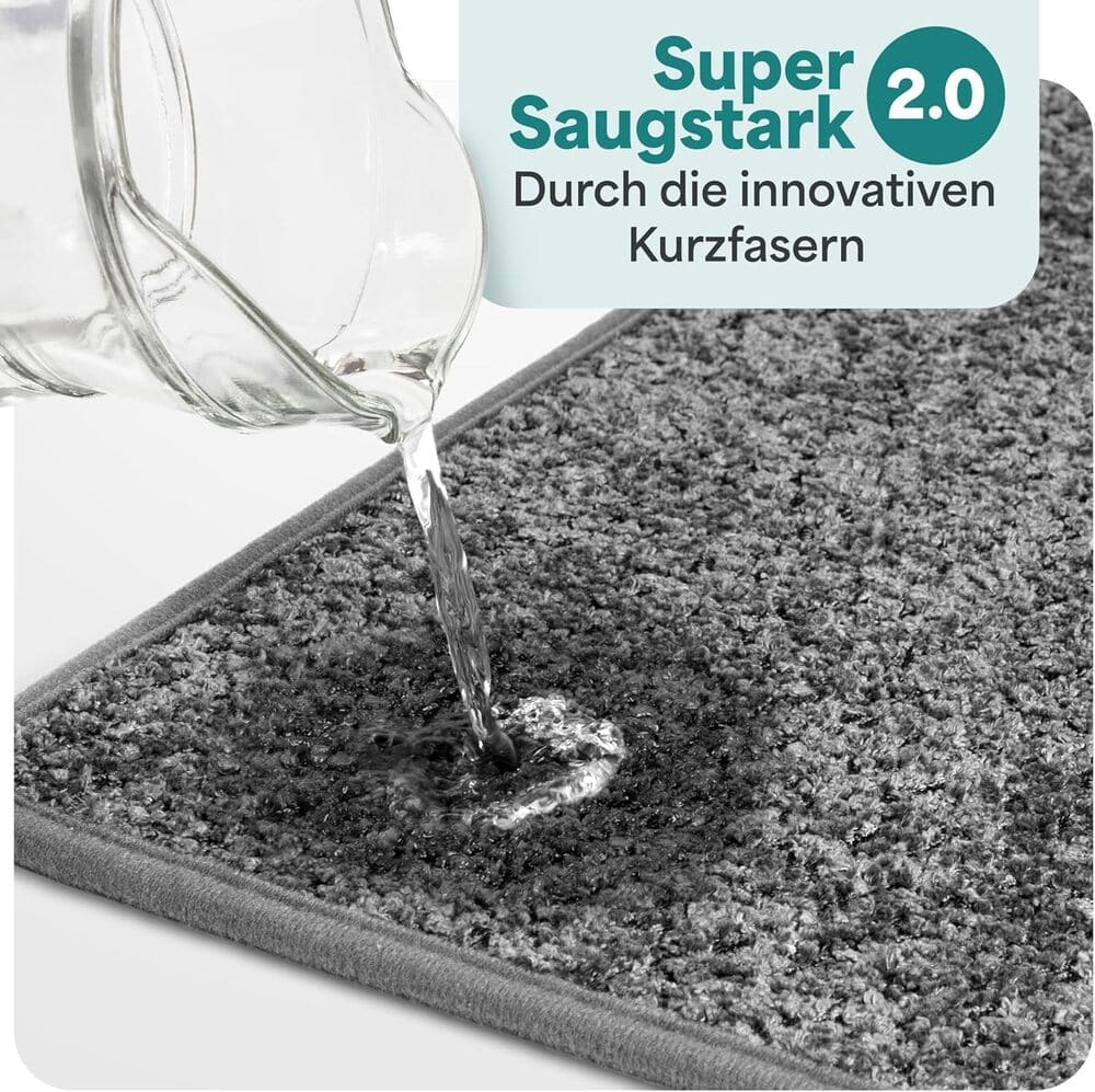 Wasser wird auf eine graue Badematte gegossen und sofort absorbiert, dank innovativer Kurzfasern mit starker Saugkraft fuer das Badezimmer