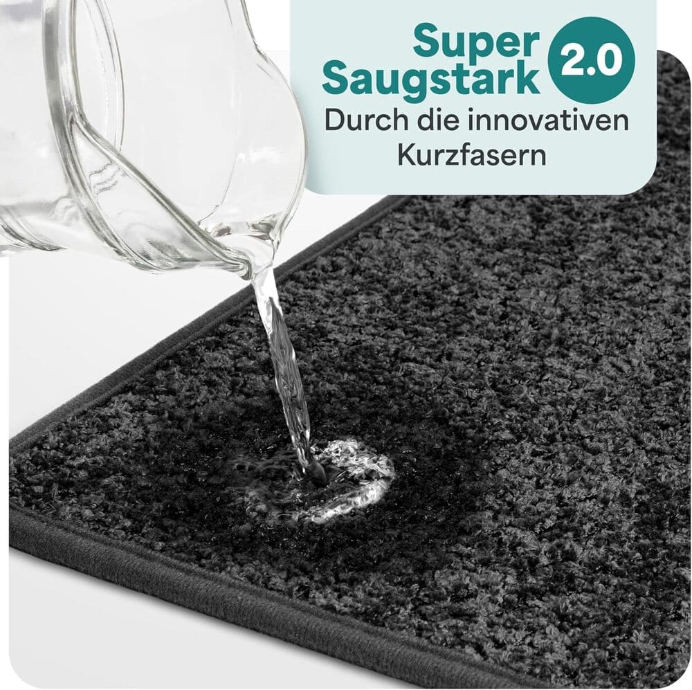 Wasser wird auf eine graue Badematte gegossen und sofort absorbiert, dank innovativer Kurzfasern mit starker Saugkraft fuer das Badezimmer