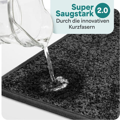 Wasser wird auf eine graue Badematte gegossen und sofort absorbiert, dank innovativer Kurzfasern mit starker Saugkraft fuer das Badezimmer