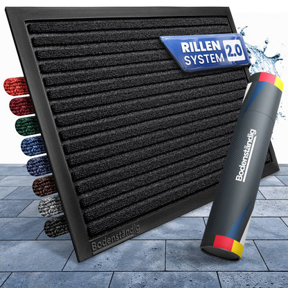 Schwarze Fußmatte mit Rillensystem 2.0, daneben Farbmuster und eine Bodenständig-Versandrolle auf Steinplatten