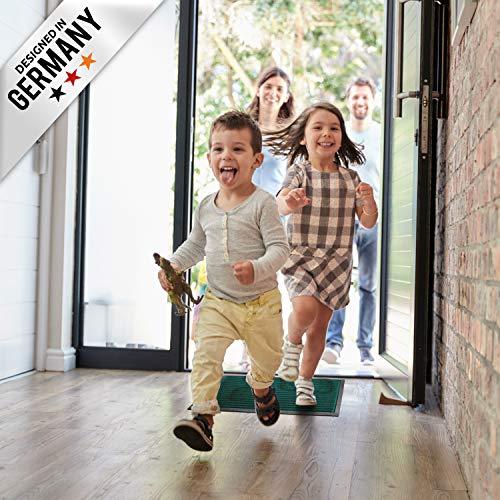 Kinder rennen in den Flur und laufen ueber eine gruene Fussmatte, waehrend Erwachsene an der offenen Haustuer stehen.
