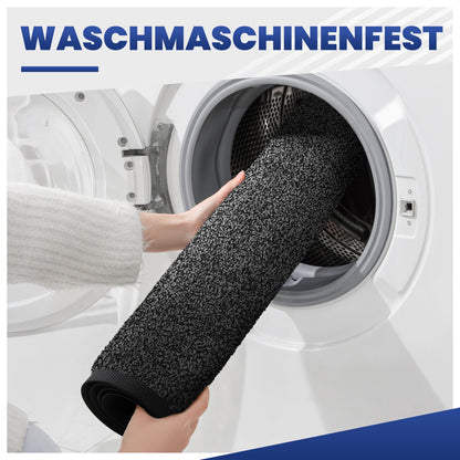 Hände legen eine aufgerollte dunkelgraue Fußmatte in eine Waschmaschine, Text: Waschmaschinenfest