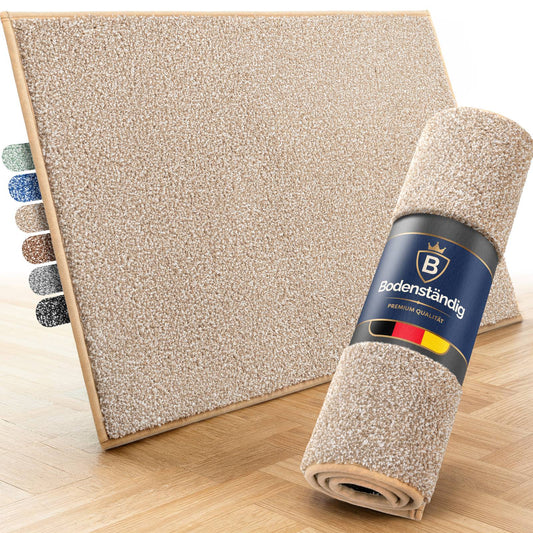 Beige Fußmatte auf Parkett, daneben eine aufgerollte Matte mit Bodenständig-Banderole und Farbmuster in sechs Farben