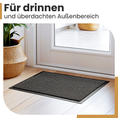 Anthrazitfarbene Fußmatte vor einer weißen Tür auf Holzboden neben einem Korb mit Pflanze, Text: Für drinnen und überdachten Außenbereich