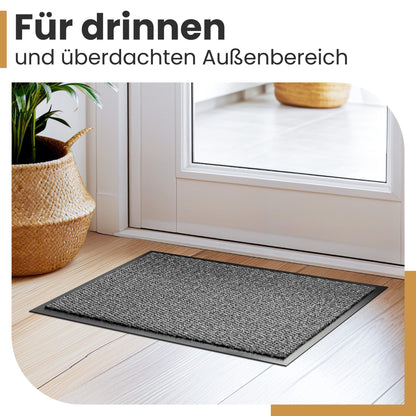 Graue Fußmatte vor einer weißen Tür im Flur, daneben ein Korb mit Pflanze, Text: Für drinnen und überdachten Außenbereich
