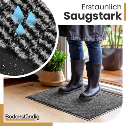 Graue Fußmatte nimmt Wasser von nassen Gummistiefeln auf; Großaufnahme mit Tropfen und Text „Erstaunlich Saugstark“