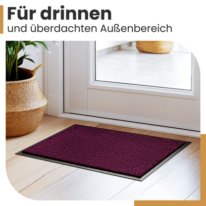 Lila Fußmatte auf Holzboden vor einer weißen Tür neben einem Korb mit Pflanze, Text „Für drinnen und überdachten Außenbereich“