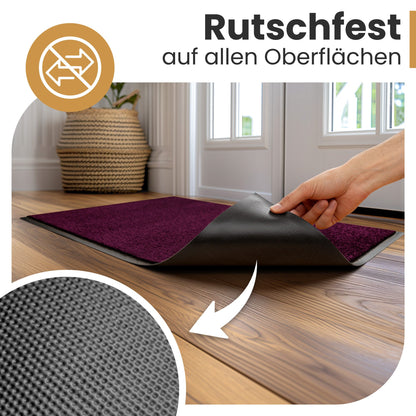 Hand hebt die Ecke einer lila Fußmatte an und zeigt die rutschfeste Rückseite mit Noppen, Text „Rutschfest auf allen Oberflächen“