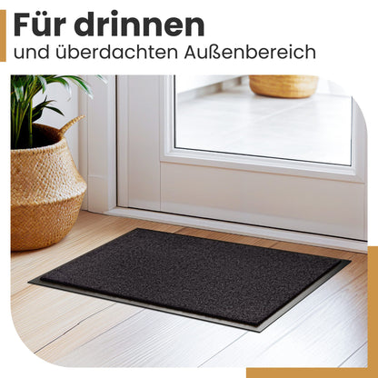 Dunkle Fußmatte vor einer weißen Tür auf hellem Holzboden, Text: Für drinnen und überdachten Außenbereich