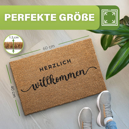 Kokos Fußmatte „Herzlich willkommen“, Maße 60 x 40 cm, Florhöhe 1,5 cm, daneben Zimmerpflanze und graue Schuhe