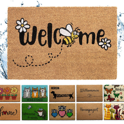 Kokos-Fußmatte mit Schriftzug „Welcome“, Biene und weißen Blüten, mit Wasserspritzern, darunter weitere Mattenmotive