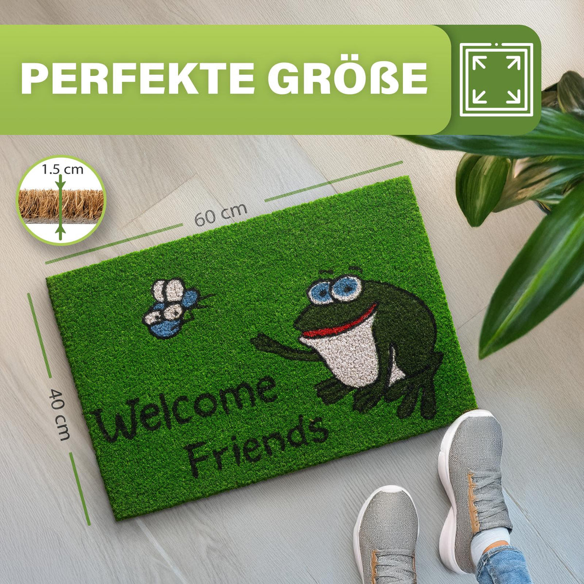 Grüne Kokosmatte „Welcome Friends“ mit Frosch, Maße 40 x 60 cm, 1,5 cm dick, neben Pflanze und Schuhen