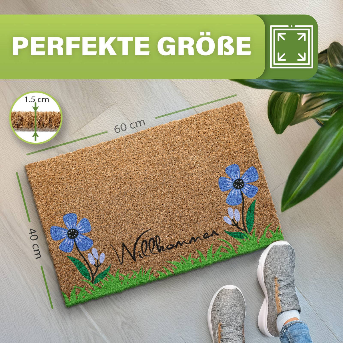 Kokosmatte „Willkommen“ mit blauen Blumen und Gras, Maße 40 x 60 cm, 1,5 cm dick, neben Pflanze und Schuhen