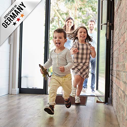 Kinder rennen in den Flur und laufen ueber eine braun Fussmatte, waehrend Erwachsene an der offenen Haustuer stehen.