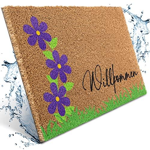 Natürliche Kokos-Fußmatte mit violetten/lila Blumen, grünem Gras und dem Schriftzug "Willkommen". Waschbar und robust.