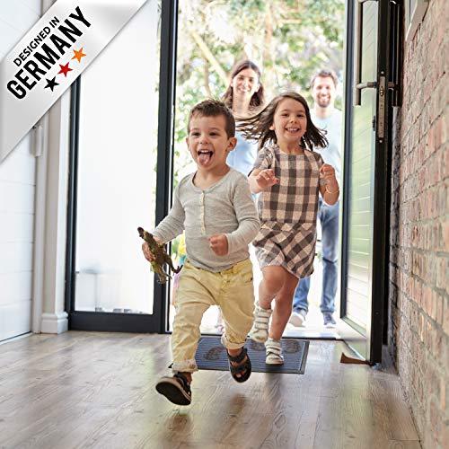 Kinder laufen lachend ueber eine Schmutzfangmatte in den Eingangsbereich, Erwachsene stehen im Hintergrund.